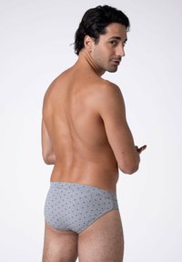 Slip da bagno grigio caratterizzato da un motivo a pois verde scuro. Il tessuto appare liscio con una vestibilità aderente, mostrando un design semplice e funzionale.