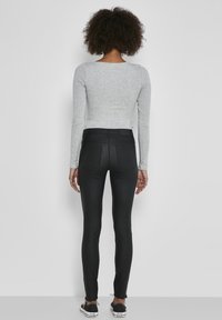 Top ajustado de manga larga gris combinado con unos vaqueros negros de talle alto. El top tiene una textura suave; los vaqueros son elegantes y tienen un detalle mínimo.