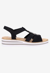 Sandale compensée noire avec des brides croisées et des accents décoratifs, une semelle texturée et une plateforme rayée blanche et grise.