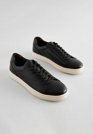 Le sneaker in pelle nera presentano una finitura testurizzata, una punta rotonda e una suola in gomma crema. I lacci si trovano sul davanti, con un design semplice e classico.