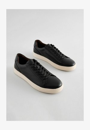 Mustad nahast tennised on tekstuuri viimistlusega, ümmarguse varbaga ja kreemja kummitaldaga. Paelad kulgevad ees, kujundus on lihtne ja klassikaline.