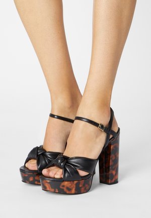 Sandales en cuir noir à plateforme avec un détail de sangle nouée et un talon bloc au motif marbré. Sangle de cheville réglable avec boucle.