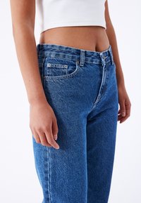 Blue denim jeans with a straight-leg cut, five-pocket design, and metal rivets. Fabric has a smooth, slightly textured finish.