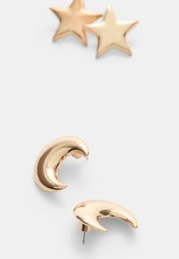 Guldmetallörhängen i en halvmåneform med en glänsande yta, tillsammans med stjärnformade studs i matchande guldton.