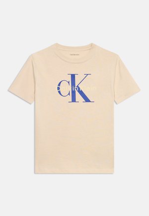 Beiges T-Shirt mit kurzen Ärmeln, großen blauen "cK"-Buchstaben und kleinem gelbem "Calvin Klein"-Schriftzug auf der Brust.