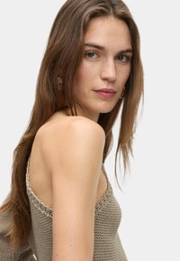 Pull en tricot beige avec de larges bretelles, présentant une surface texturée et une coupe décontractée, mettant en valeur un détail d'épaule.
