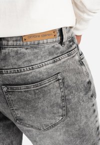 Harmaat farkut, joissa on haalistunut ombre-efekti. Vyötäröllä on vaaleanruskea nahkatagi, jossa lukee "ombre denim", ja hopeiset metalliosat korostavat tyyliä.