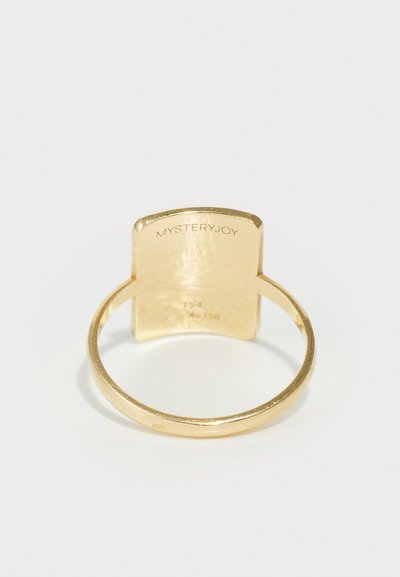 Gold ring with a smooth band and a flat, rounded top. Engraved details read "MYSTERYJOY" and "Ag750." Simple, modern design.