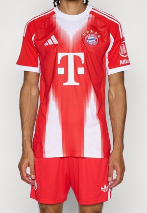 Personne portant un maillot de football rouge et blanc du FC Bayern Munich et un short rouge assorti avec les logos Adidas et du sponsor.