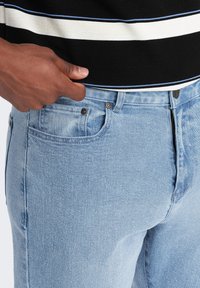 Jeans de denim azul claro con un corte clásico, que presentan un bolsillo frontal, detalles de botones de metal y una textura ligeramente desgastada.