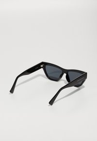 Ochelari de soare negri tip cat-eye, cu lentile întunecate, cadru dinplastic lucios și brațe subțiri cu detalii logo pe o parte.