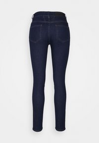 Jean skinny bleu foncé vu de dos, avec deux poches arrière, des jambes ajustées et des coutures visibles, présenté sur un fond blanc uni.