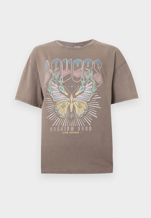 T-shirt marron surdimensionné avec un grand motif coloré de papillon, le texte « WAVES » au-dessus, et le texte « Stadium Tour live concert » en dessous à l'avant.