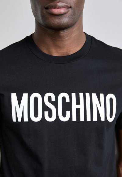 Svart bomull T-skjorte med fet hvit "MOSCHINO" tekst på brystet, rund halslinning og kortermet. Glatt tekstur.