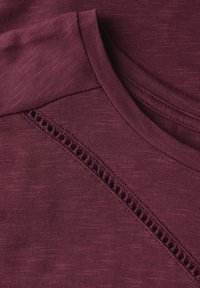 Haut bordeaux avec un tricot texturé et un décolleté arrondi, orné d'une bordure en dentelle détaillée le long de la couture de l'épaule.
