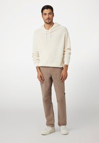 Cremefarvet hoodie med struktur og snoretræk, parret med lysebrune cargo-bukser og hvide sneakers. Enkel, afslappet outfit med funktionelle elementer.
