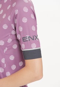Kurzarmpullover für Radfahrer in helllila mit weißem Punkte-Muster, ausgestattet mit einem grauen Bündchen und dem "ENX"-Logo auf dem Arm. Glatte Stoffstruktur.