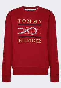 Red sweatshirt featuring a crew neckline, long sleeves, and a graphic design with "TOMMY HILFIGER" and a rope pattern in contrasting colors.