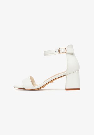 Sandalia blanca de punta abierta con tacón ancho y correa ajustable en el tobillo con hebilla dorada, mostrada de perfil sobre un fondo blanco.