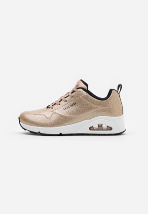 Baskets Skechers en or rose métallique avec doublure noire, semelle blanche amortie par air, semelle extérieure noire et languette au talon.
