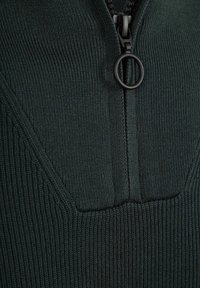 Dunkelgrüner Strickpullover mit einem halben Reißverschluss am Kragen, der vertikale Rippungen und einen strukturierten Körper aufweist. Zirkuläres Detail am Reißverschluss.