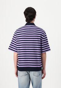 Kortermet poloskjorte i lilla og marineblå striper, med krage og solid marineblå kant. Laget av teksturert bomullsstoff.