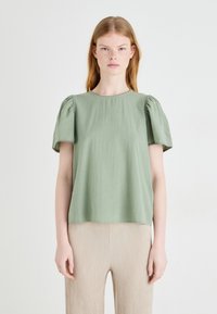 Bluzka s kratkimi rokavi, svetlo zelena, z napihnjenimi rokavi in okroglim izrezom. Narejena iz mehkega blaga z rahlo teksturirano površino.