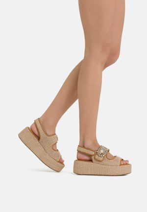Sandali con zeppa dalla texture intrecciata, colore marrone chiaro, design a punta aperta e fibbia decorativa sulla tracolla. Suola piattaforma per un'altezza extra.
