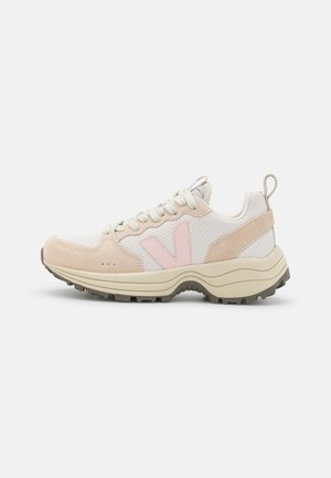 Chaussure de sport blanche et beige avec logo rose "V", semelle épaisse avec une profonde bande de roulement, tissu en mesh, accents en daim et languette au talon.