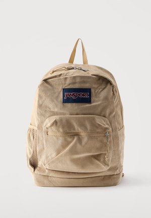 Zaino Jansport in velluto a coste beige con tasca frontale con cerniera, tasca laterale in rete e maniglia superiore su sfondo bianco.