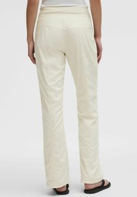 Pantalone boje krem, lagani s teksturiranom tkaninom, elastičnim pojasom i ravnim krojem. Ima bočne šavove i ležeran kroj.