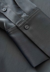 Poignet de chemise en satin noir à texture lisse, doté de deux boutons ronds noirs et d'un détail de surpiqûre.
