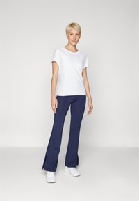 White athletic top with mesh side panels, paired with navy flared leggings featuring side splits. White sneakers complete the outfit.