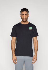 Μαύρο βαμβακερό T-shirt με κοντά μανίκια, με πολύχρωμο λογότυπο "Just Do It" της Nike στο αριστερό στήθος. Λείος υφής και άνετη εφαρμογή.