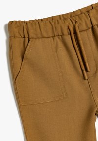 Beige bomuldsbukser med elastisk talje, snøre til lukning og sidelommer med en tekstureret finish.