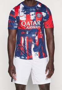 Fotbalový dres Nike má modrou základnu s červenými a bílými štětcovými vzory, logo na levé hrudi a design s kulatým výstřihem.