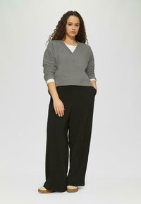 Grauer V-Ausschnitt-Pullover mit gerippten Details, kombiniert mit locker sitzenden schwarzen Hosen. Das Model trägt beige Slipper. Einfaches, modernes Design.