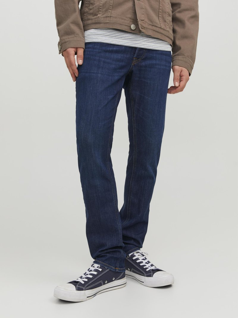 Mørkeblå jeans i slim fit, med klassisk femlommers design og diskrete sting. Båret med en lys stripete skjorte og casual sneakers.