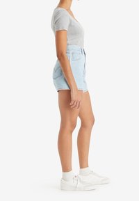 Light denim shorts with high waist, front button closure, and cut-off hem. Gray ribbed short-sleeve top paired with white sneakers.