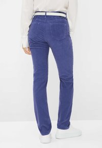Pantaloni in corduroy viola con una vestibilità dritta, dotati di tasche posteriori e abbinati a sneakers bianche. La vita è accentuata da una cintura bianca.