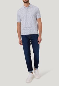 Lichtgrijze marl polo met korte mouwen, drie knopenlijst en een zachte textuur, gecombineerd met donkerblauwe tapered jeans en witte sneakers.