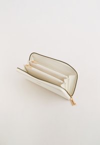 Witte ritsportemonnee met gouden hardware-accenten, meerdere kaartsleuven en een gestructureerde afwerking. Het interieur is gevoerd in een neutrale kleur.
