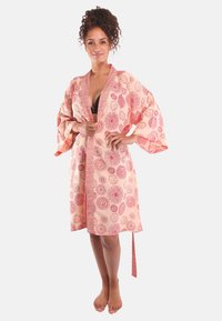 Kimono-achtige badjas van lichtroze stof met rode cirkelvormige patronen, brede mouwen, een strikceintuur en zijslits. Soepele textuur, casual ontwerp.