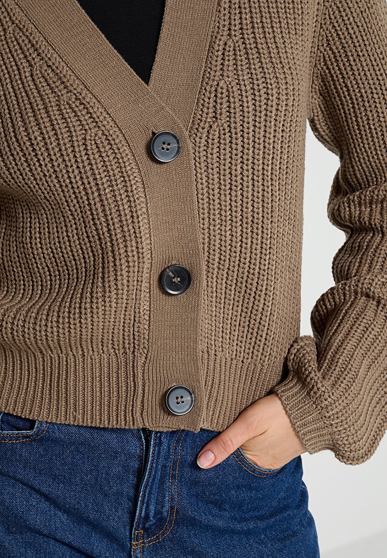 Braune Strickjacke mit V-Ausschnitt, gerippten Abschlüssen und vier schwarzen Knöpfen auf der Vorderseite. Der strukturierte Stoff zeigt ein gewebtes Muster.