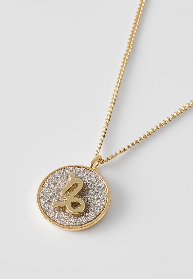 Collana dorata con un pendente circolare. Il pendente presenta una superficie in argento testurizzato e un simbolo dorato in rilievo. Il design della catena è intrecciato.
