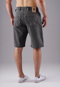 Man wearing dark gray denim shorts and white low-top Converse sneakers, standing against a plain light gray background.