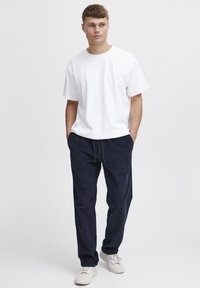 White cotton t-shirt with a crew neckline, paired with navy corduroy pants featuring a drawstring waist, and white sneakers.