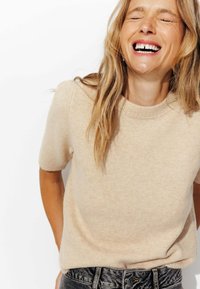 Pull beige à manches courtes avec un motif en tricot texturé et un col rond, associé à un jean en denim foncé.