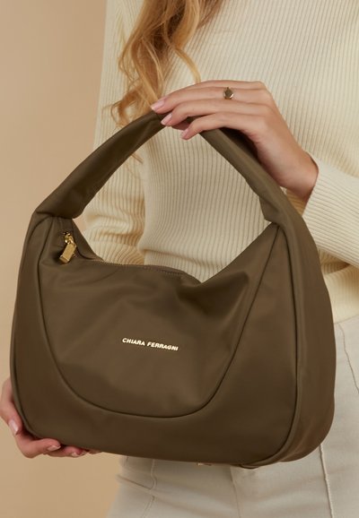 Olijfgroene handtas van zacht materiaal met een gebogen silhouet, gouden hardware en een logo-accent. Korte riem voor het dragen over de schouder.