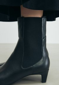 Bottines noires en cuir lisse avec des panneaux latéraux élastiques et un talon effilé pour une silhouette ajustée.
